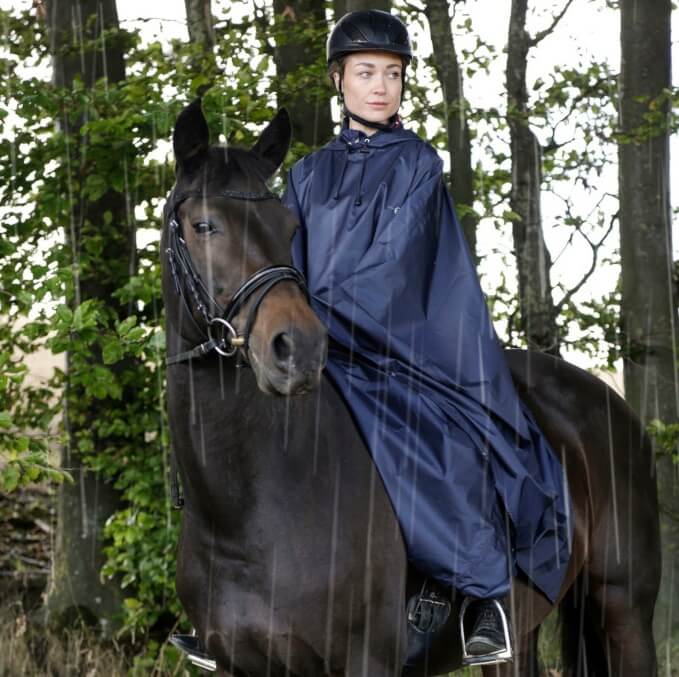 Reiterin mit Regenponcho sitzt auf Pferd