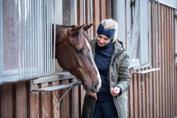 Reiterin streichelt Pferd in Box